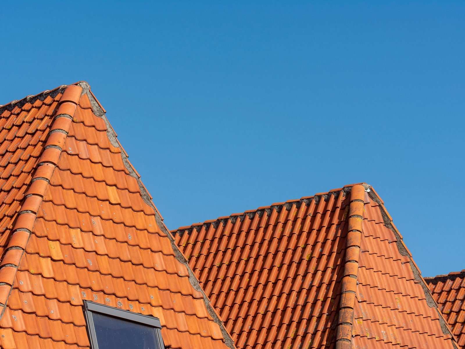 Orange tile roof gables with a skylight under a blue sky